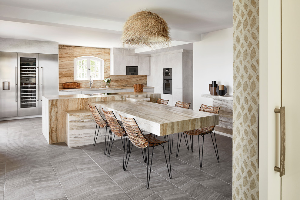 This is an example of an expansive beach style l-shaped kitchen with marble benchtops, with island, grey floor, beige benchtop, flat-panel cabinets, grey cabinets, beige splashback, stone slab splashback and stainless steel appliances.