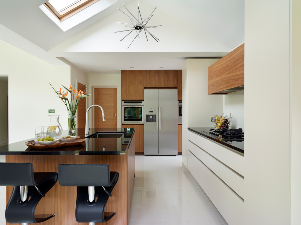 This is an example of a large contemporary open plan kitchen in London with flat-panel cabinets, medium wood cabinets, granite benchtops and with island.