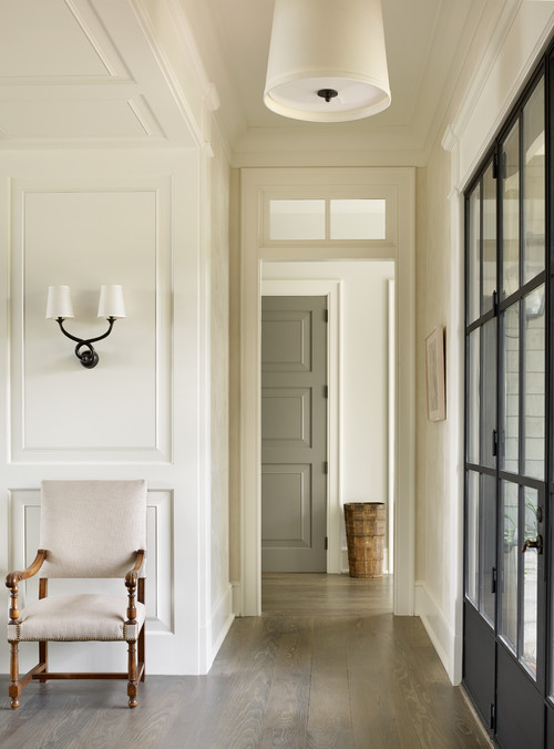 A long hallway with a white chair by the wall and wall sconce above the chair.