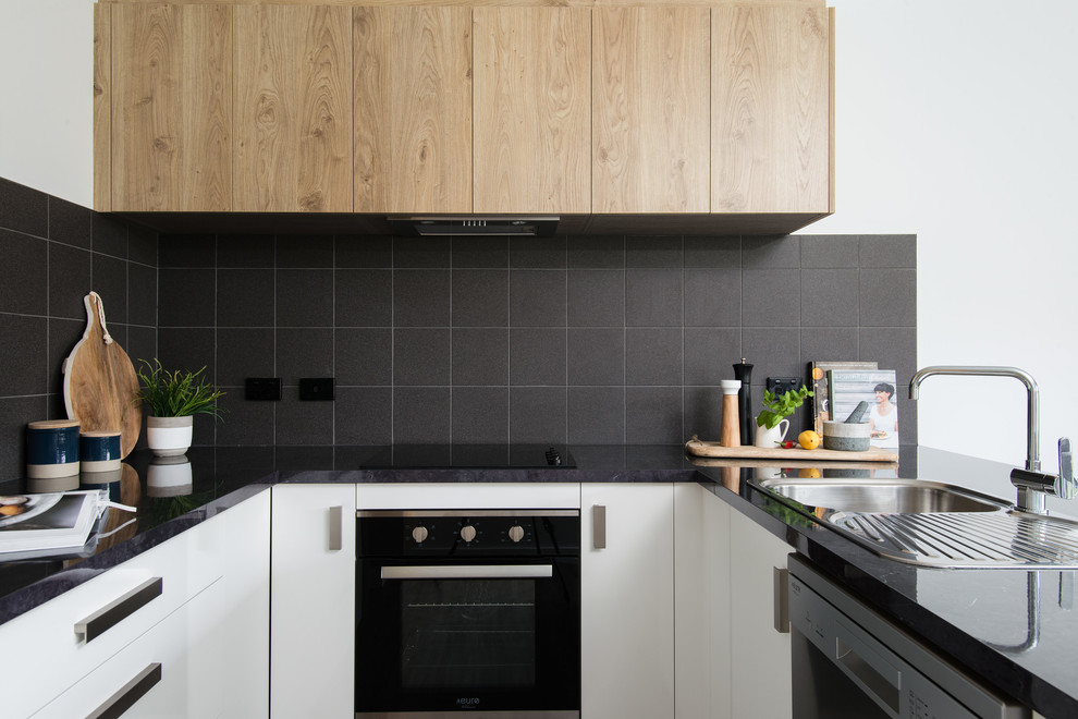 Inspiration for a small modern u-shaped open plan kitchen in Other with a drop-in sink, white cabinets, laminate benchtops, black splashback, ceramic splashback, black appliances, vinyl floors, no island, brown floor and black benchtop.