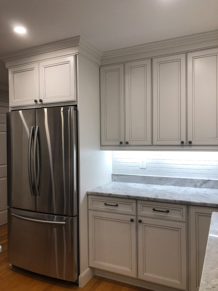 Large transitional l-shaped medium tone wood floor and brown floor open concept kitchen photo in Boston with an undermount sink, recessed-panel cabinets, white cabinets, quartz countertops, white backsplash, subway tile backsplash, stainless steel appliances, an island and multicolored countertops