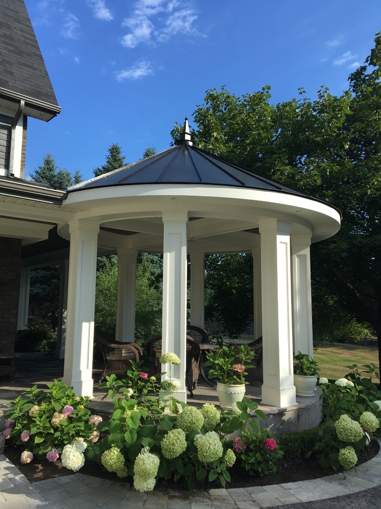 Photo of a mid-sized country side yard verandah in Toronto with natural stone pavers.