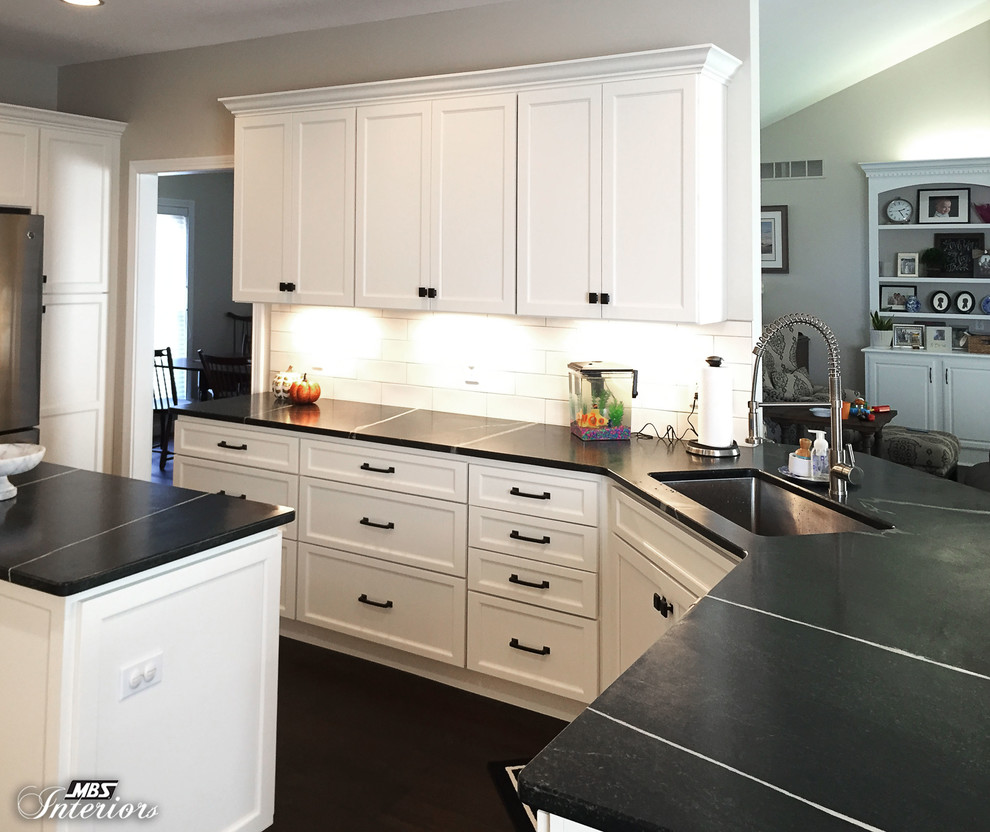 Example of a mid-sized transitional u-shaped dark wood floor and brown floor eat-in kitchen design with an undermount sink, recessed-panel cabinets, white cabinets, soapstone countertops, white backsplash, subway tile backsplash, stainless steel appliances and an island