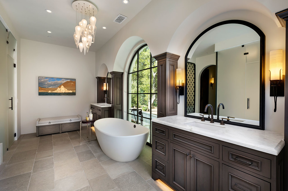 Inspiration for a large mediterranean master bathroom in Other with dark wood cabinets, a freestanding tub, white walls, limestone floors, an undermount sink, marble benchtops, grey floor, white benchtops and recessed-panel cabinets.
