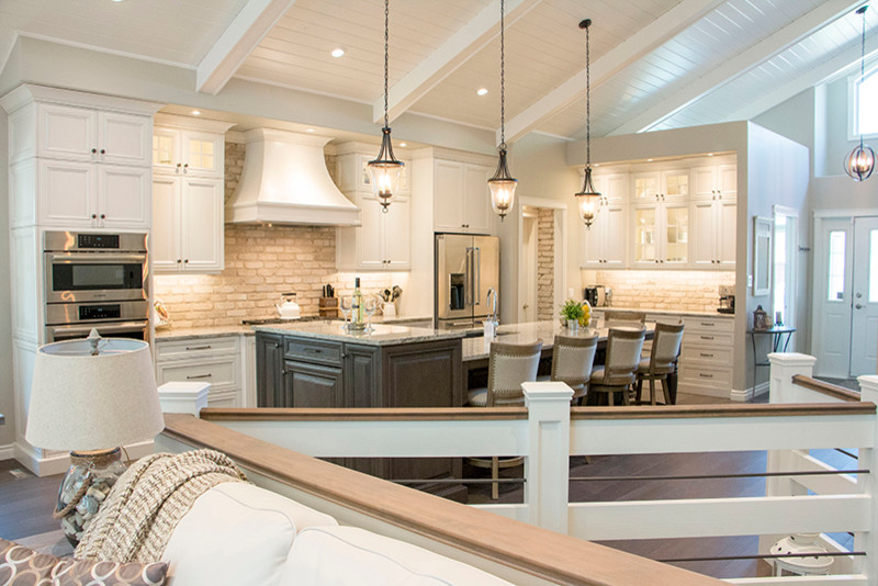 Eat-in kitchen - large transitional l-shaped eat-in kitchen idea with a double-bowl sink, shaker cabinets, white cabinets, beige backsplash, stainless steel appliances and an island