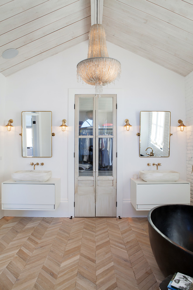Inspiration for a mid-sized country master bathroom in Orange County with flat-panel cabinets, white cabinets, a freestanding tub, white walls, light hardwood floors, a vessel sink, beige floor, white tile and solid surface benchtops.