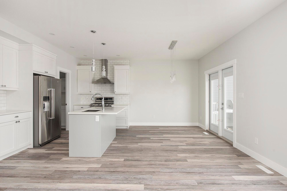 Mid-sized transitional l-shaped medium tone wood floor and brown floor open concept kitchen photo in Calgary with an undermount sink, shaker cabinets, white cabinets, quartzite countertops, white backsplash, subway tile backsplash, stainless steel appliances, an island and white countertops