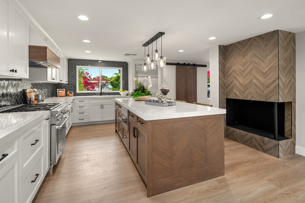 Inspiration for a medium sized country l-shaped kitchen/diner in Orange County with a belfast sink, shaker cabinets, white cabinets, engineered stone countertops, blue splashback, ceramic splashback, stainless steel appliances, laminate floors and an island.