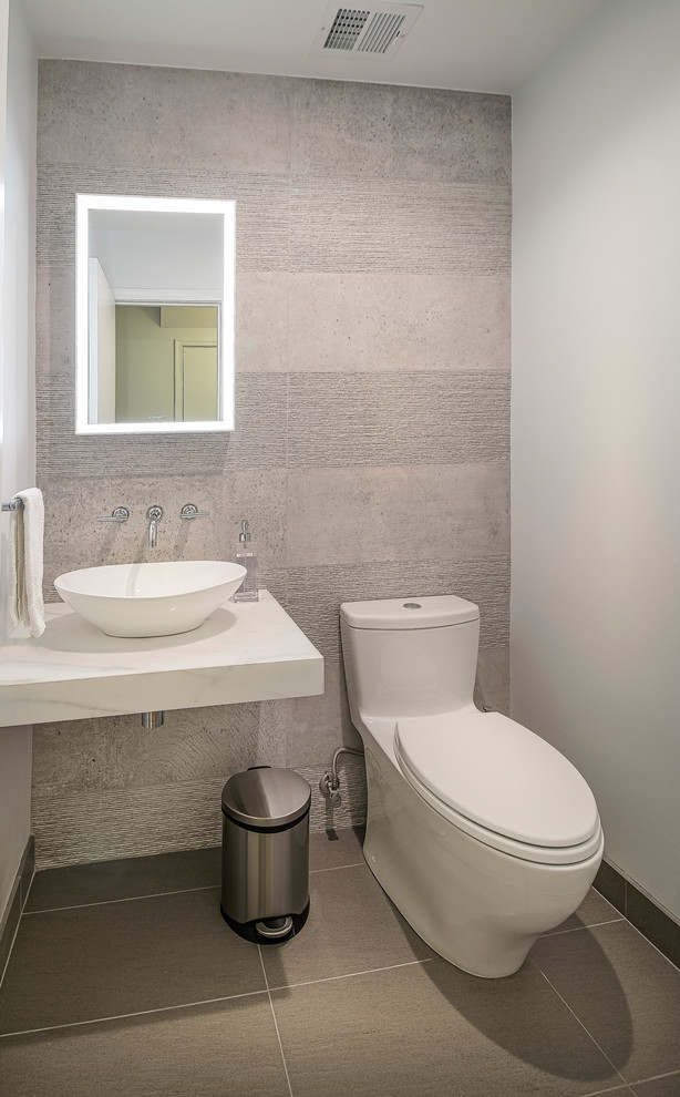 This is an example of a small contemporary powder room in DC Metro with a one-piece toilet, beige tile, cement tile, beige walls, laminate floors, a vessel sink, marble benchtops, beige floor and white benchtops.