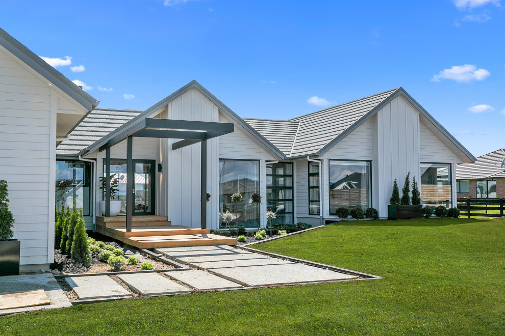 Aménagement d'une grande façade de maison blanche en bois et planches et couvre-joints de plain-pied avec un toit à quatre pans, un toit en shingle et un toit gris.