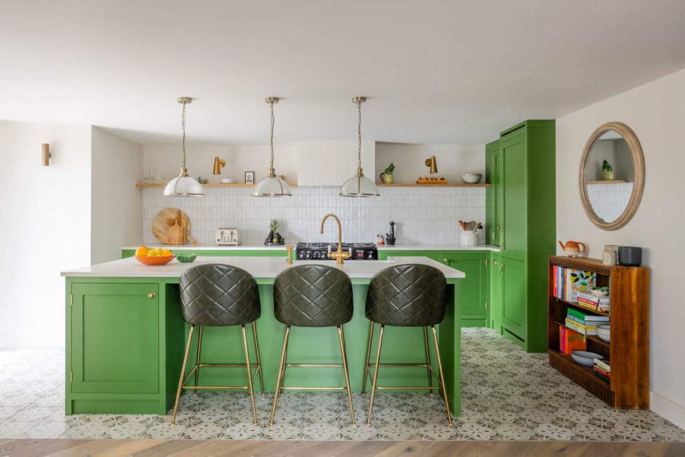 Design ideas for a mid-sized eclectic l-shaped eat-in kitchen in Other with a farmhouse sink, shaker cabinets, green cabinets, quartzite benchtops, white splashback, ceramic splashback, black appliances, porcelain floors, with island, multi-coloured floor and white benchtop.