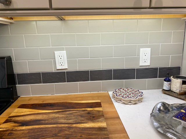 Inspiration for a mid-sized transitional u-shaped porcelain tile and gray floor eat-in kitchen remodel in Burlington with a farmhouse sink, recessed-panel cabinets, white cabinets, quartz countertops, gray backsplash, subway tile backsplash, stainless steel appliances and white countertops