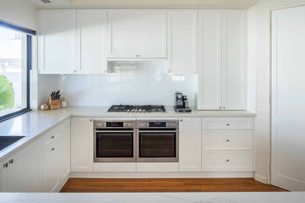This is an example of a transitional kitchen in Perth with a drop-in sink, shaker cabinets, white cabinets, quartz benchtops, white splashback, subway tile splashback, stainless steel appliances and white benchtop.