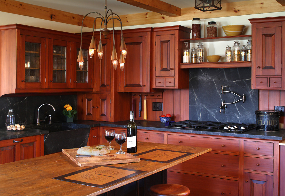 Country kitchen in Portland Maine with a farmhouse sink, raised-panel cabinets, dark wood cabinets, black splashback and stone slab splashback.