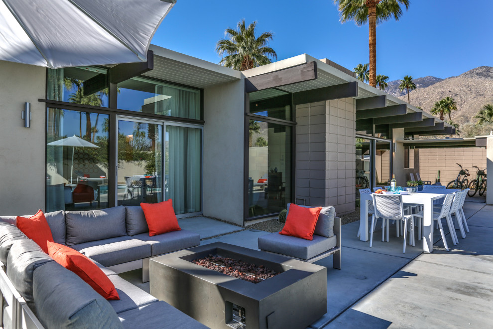 Photo of a midcentury backyard patio in Other with a fire feature, concrete slab and a roof extension.
