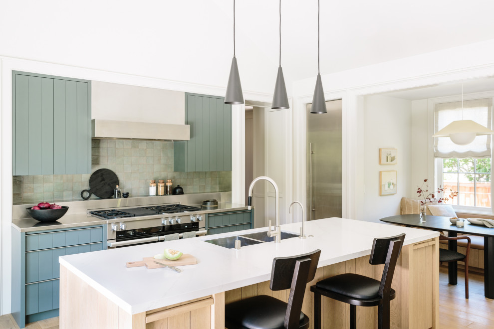 This is an example of a mid-sized country galley eat-in kitchen in San Francisco with a double-bowl sink, blue cabinets, stainless steel benchtops, grey splashback, stainless steel appliances, grey benchtop, flat-panel cabinets, glass tile splashback, multiple islands and vaulted.