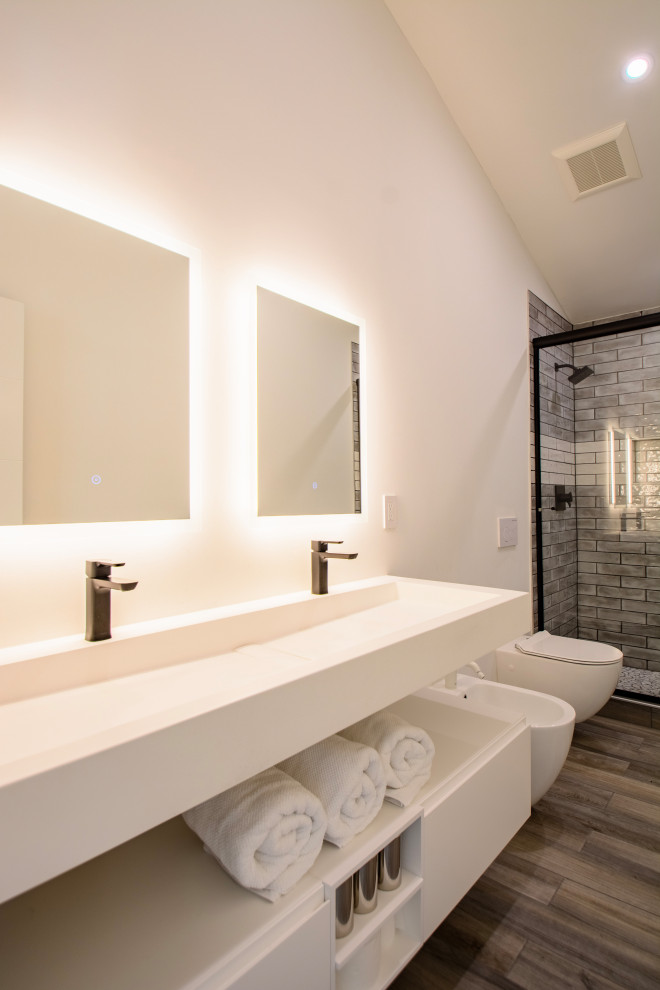 Modern kids bathroom in Denver with flat-panel cabinets, white cabinets, an alcove shower, a bidet, gray tile, subway tile, white walls, wood-look tile, a wall-mount sink, solid surface benchtops, brown floor, a sliding shower screen, white benchtops, a niche, a double vanity, a floating vanity and vaulted.