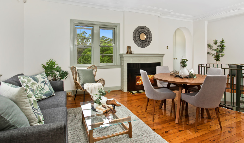 This is an example of a small transitional dining room in Sydney with medium hardwood floors, a standard fireplace, a brick fireplace surround, white walls and brown floor.