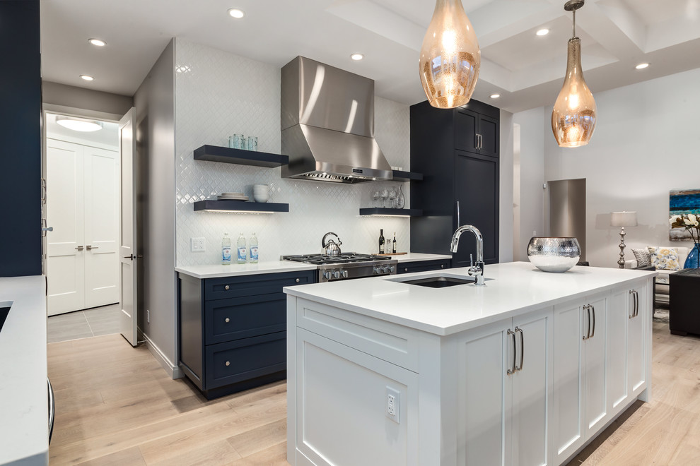 Kitchen - transitional u-shaped light wood floor kitchen idea in Calgary with an undermount sink, shaker cabinets, blue cabinets, quartzite countertops, white backsplash, porcelain backsplash, stainless steel appliances and an island