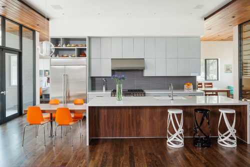 Contemporary kitchen with light-gray flat-panel RTA cabinets, a walnut waterfall island, gray linear backsplash, stainless appliances, and orange dining chairs.