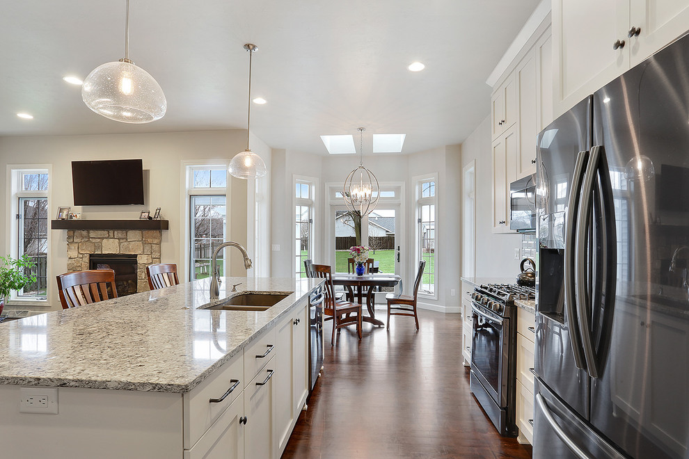 Example of a mid-sized transitional medium tone wood floor and brown floor open concept kitchen design with an undermount sink, flat-panel cabinets, white cabinets, granite countertops, ceramic backsplash, stainless steel appliances, an island and multicolored countertops