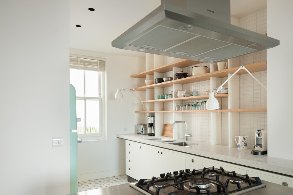This is an example of a mid-sized transitional single-wall open plan kitchen in London with a double-bowl sink, shaker cabinets, white cabinets, solid surface benchtops, white splashback, ceramic splashback, stainless steel appliances, ceramic floors and with island.