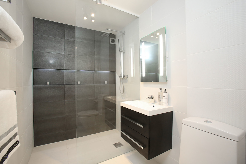 Small modern bathroom in London with a wall-mount sink, dark wood cabinets, a two-piece toilet, white tile, ceramic tile, ceramic floors, a curbless shower and flat-panel cabinets.