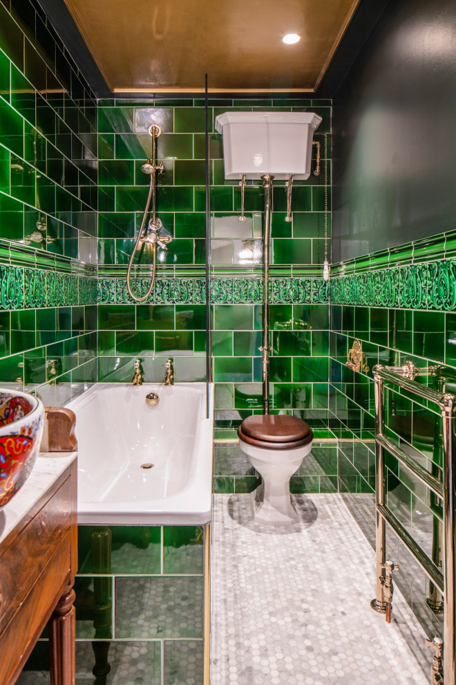 This is an example of a traditional bathroom in London with flat-panel cabinets, medium wood cabinets, a corner tub, a shower/bathtub combo, a two-piece toilet, green tile, subway tile, black walls, mosaic tile floors, a vessel sink, white floor, an open shower, white benchtops, a single vanity and a freestanding vanity.