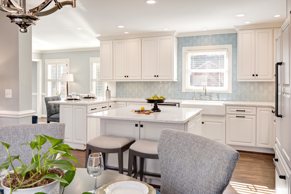 Eat-in kitchen - mid-sized transitional u-shaped medium tone wood floor and brown floor eat-in kitchen idea with a farmhouse sink, raised-panel cabinets, white cabinets, quartz countertops, blue backsplash, porcelain backsplash, paneled appliances and an island