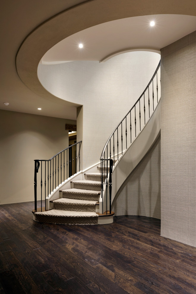 Photo of a large transitional wood curved staircase in DC Metro with carpet risers, metal railing and wallpaper.