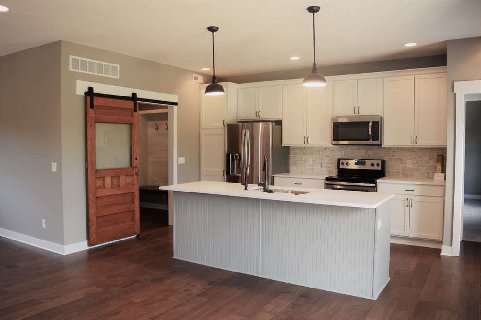 Mid-sized transitional galley medium tone wood floor and brown floor open concept kitchen photo with a double-bowl sink, raised-panel cabinets, white cabinets, multicolored backsplash, brick backsplash, stainless steel appliances and an island