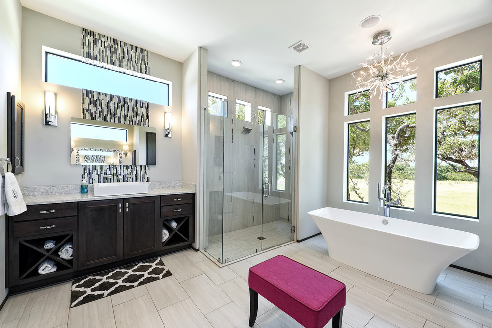 Photo of a transitional master bathroom in Austin with recessed-panel cabinets, black cabinets, a freestanding tub, a corner shower, grey walls, a vessel sink, grey floor and a hinged shower door.