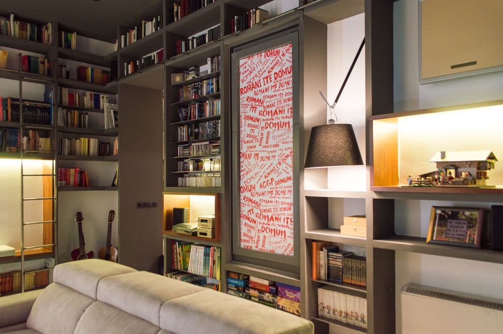 Foto de biblioteca en casa abierta actual de tamaño medio sin chimenea con paredes blancas, suelo de madera clara y pared multimedia