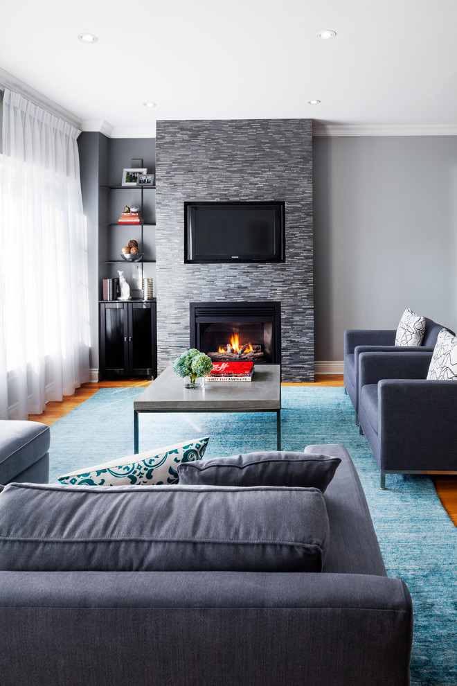 This is an example of a mid-sized transitional open concept living room in Toronto with grey walls, medium hardwood floors, a tile fireplace surround and a wall-mounted tv.