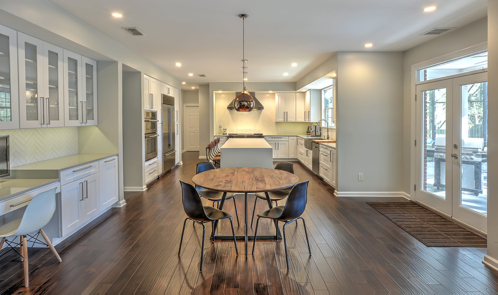 Photo of a large transitional u-shaped eat-in kitchen in Jacksonville with recessed-panel cabinets, white cabinets, stainless steel appliances, dark hardwood floors, with island, a farmhouse sink, brown floor, white splashback, ceramic splashback and quartzite benchtops.
