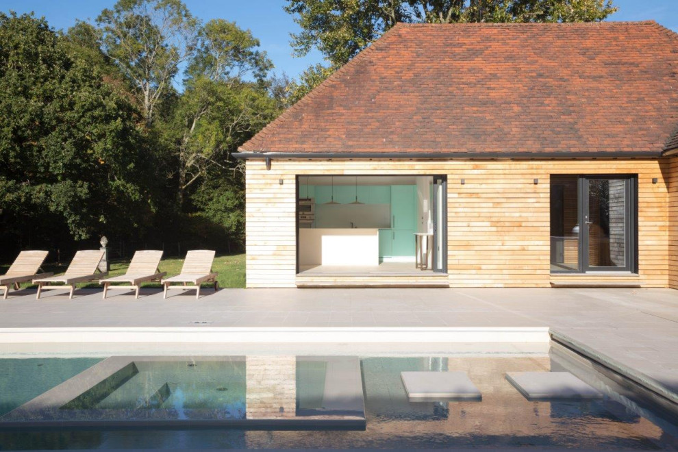 Photo of a mid-sized contemporary backyard rectangular lap pool in Sussex with a pool house and natural stone pavers.