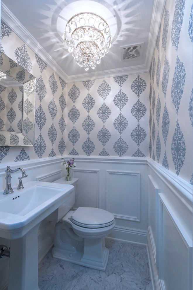 Small transitional powder room in New York with a one-piece toilet, white walls, marble floors and a pedestal sink.