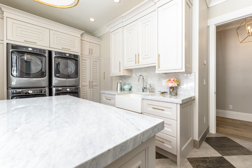 Photo of a large transitional u-shaped dedicated laundry room in Salt Lake City with a farmhouse sink, recessed-panel cabinets, beige cabinets, beige walls, a stacked washer and dryer, multi-coloured floor, white benchtop and marble benchtops.