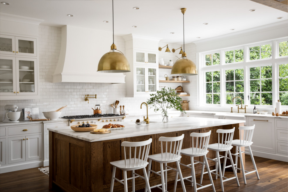 Open concept kitchen - large transitional u-shaped medium tone wood floor, brown floor and exposed beam open concept kitchen idea with a farmhouse sink, shaker cabinets, white cabinets, marble countertops, white backsplash, subway tile backsplash, paneled appliances, an island and white countertops