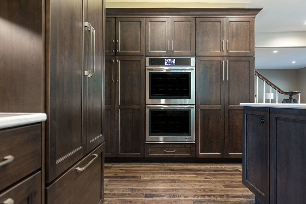 Example of a large transitional l-shaped brown floor and medium tone wood floor eat-in kitchen design with an undermount sink, flat-panel cabinets, dark wood cabinets, white backsplash, an island, marble countertops, ceramic backsplash, stainless steel appliances and white countertops