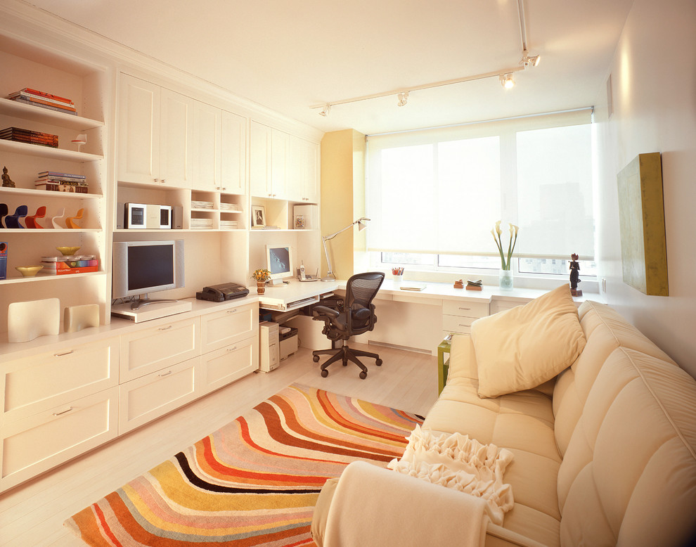 This is an example of a contemporary home office in New York with a built-in desk and beige floor.