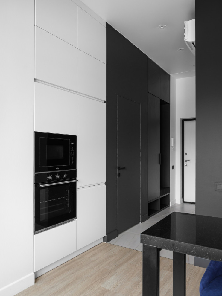 This is an example of a small contemporary galley open plan kitchen in Other with an undermount sink, flat-panel cabinets, white cabinets, quartz benchtops, white splashback, black appliances, laminate floors, no island, beige floor and black benchtop.
