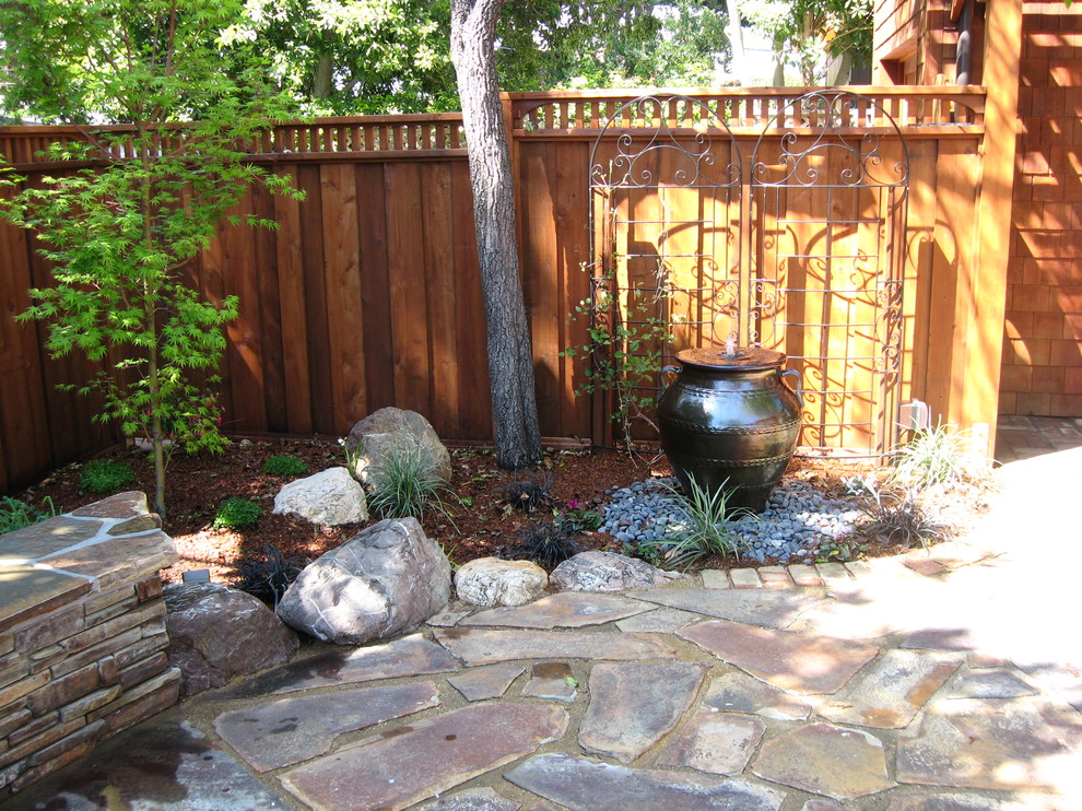 This is an example of a small mediterranean courtyard patio in San Francisco with a water feature, natural stone pavers and no cover.