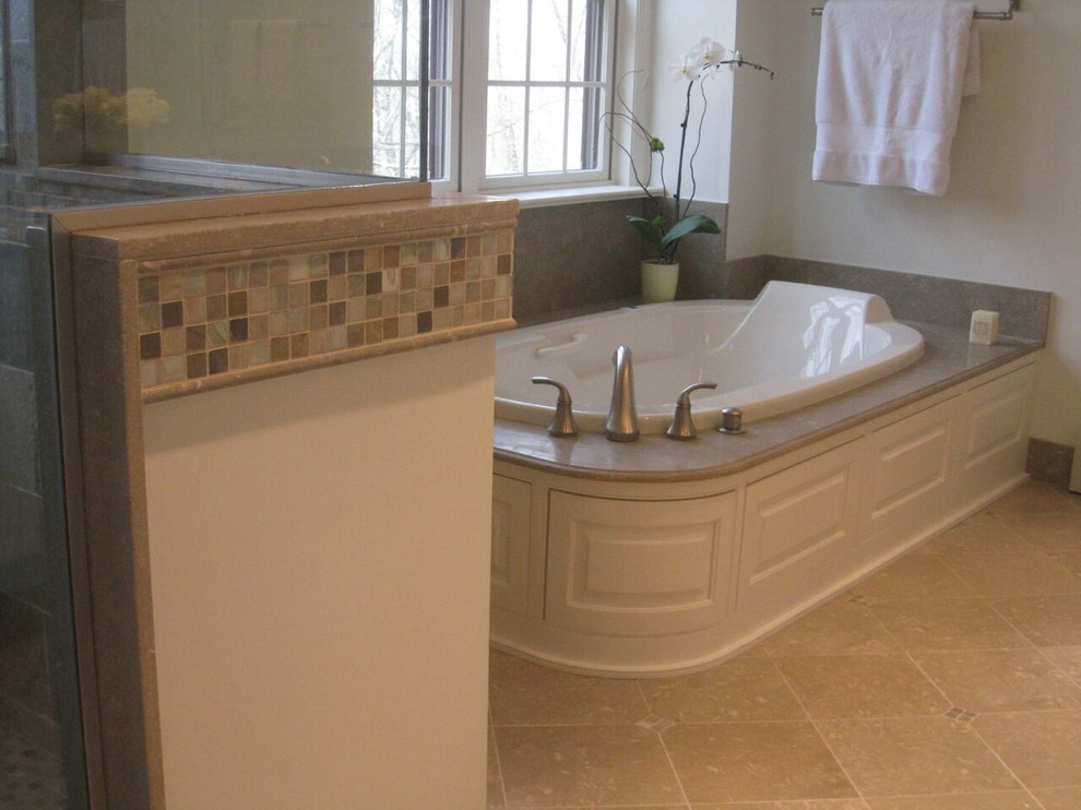Photo of a large traditional master bathroom in New York with raised-panel cabinets, white cabinets, a drop-in tub, a corner shower, beige tile, stone tile, beige walls, travertine floors, an undermount sink and limestone benchtops.