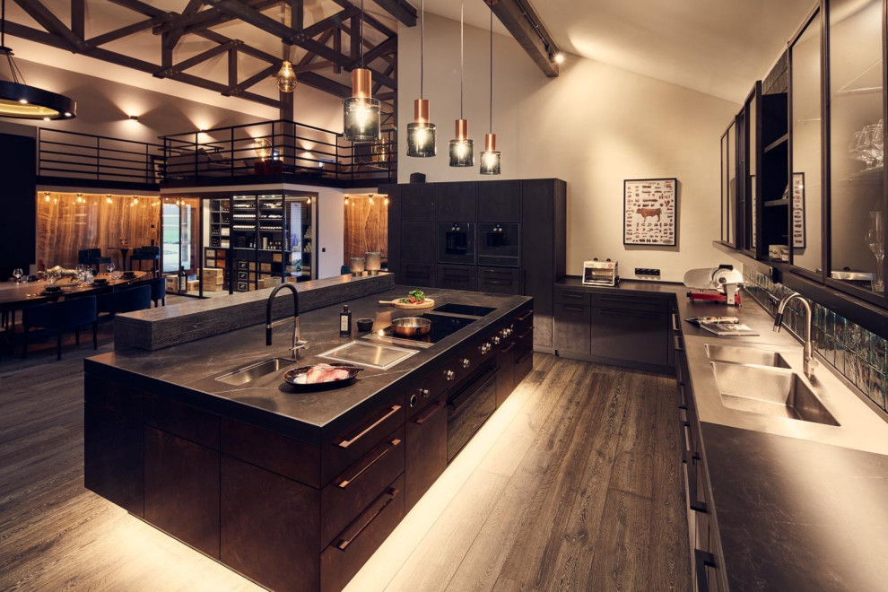 Photo of a large industrial u-shaped open plan kitchen in Munich with an undermount sink, flat-panel cabinets, tile benchtops, green splashback, subway tile splashback, dark hardwood floors, with island, black benchtop and exposed beam.