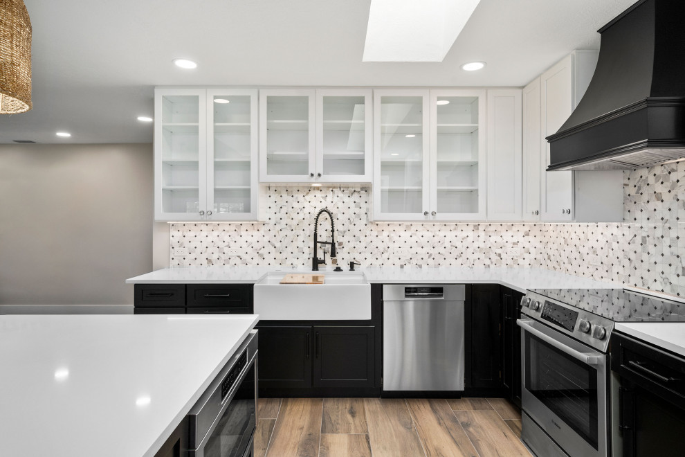 This is an example of a mid-sized modern l-shaped eat-in kitchen in Atlanta with a farmhouse sink, shaker cabinets, black cabinets, granite benchtops, white splashback, granite splashback, stainless steel appliances, painted wood floors, with island and brown floor.