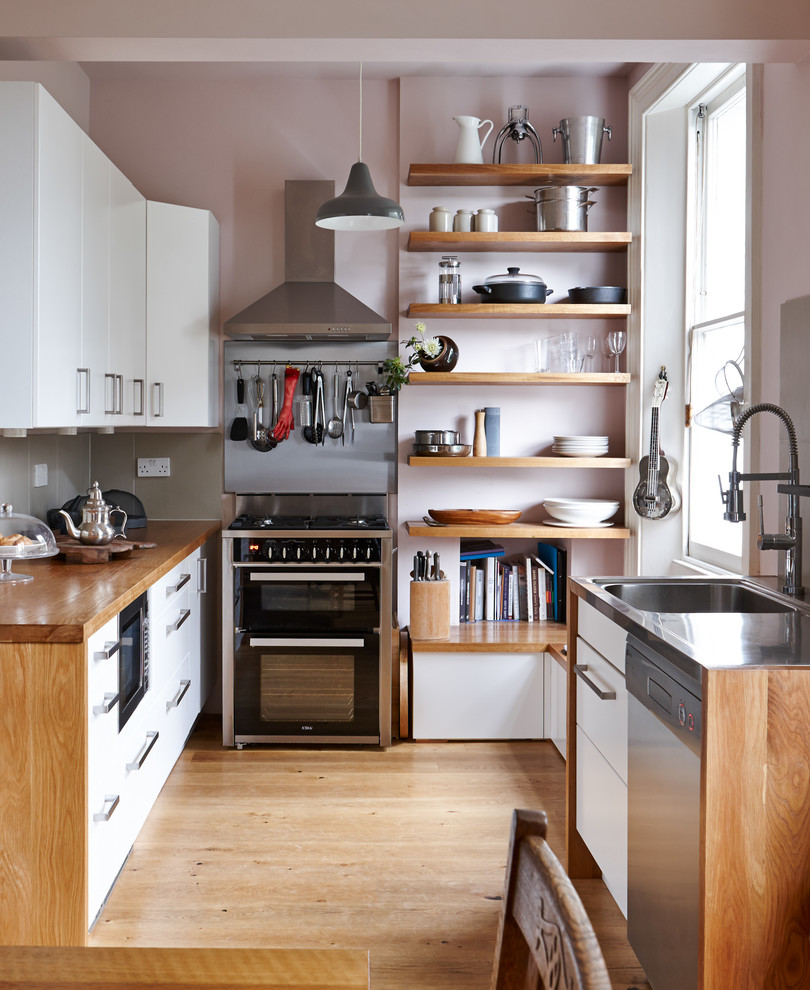 Inspiration for a small contemporary kitchen in London with flat-panel cabinets, white cabinets, wood benchtops, grey splashback, porcelain splashback, medium hardwood floors, no island and black appliances.