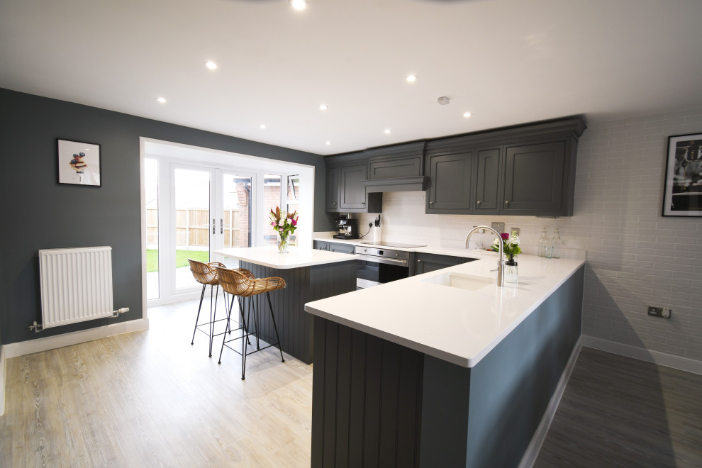 Inspiration for a large traditional l-shaped kitchen/diner in Essex with a single-bowl sink, shaker cabinets, grey cabinets, quartz worktops, black appliances, an island and white worktops.