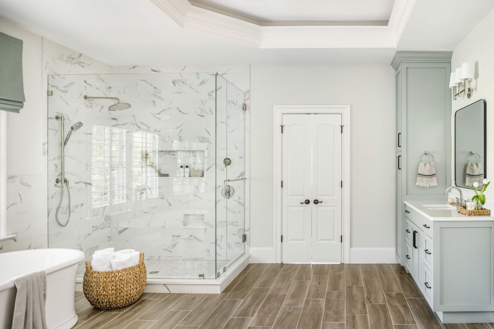 This is an example of a large transitional master bathroom in Charlotte with shaker cabinets, green cabinets, a freestanding tub, white tile, porcelain tile, grey walls, porcelain floors, an undermount sink, engineered quartz benchtops, brown floor, a hinged shower door, white benchtops, a niche, a single vanity and a built-in vanity.