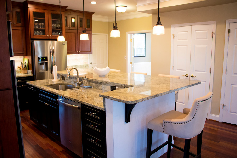 Example of a large transitional l-shaped dark wood floor and brown floor enclosed kitchen design in DC Metro with a double-bowl sink, raised-panel cabinets, dark wood cabinets, granite countertops, beige backsplash, limestone backsplash, stainless steel appliances and an island